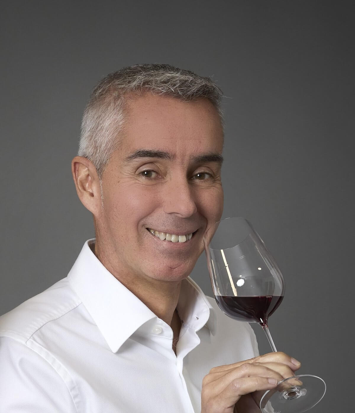 Gros plan de Damien Delattre, expert en œnologie en Bourgogne, souriant avec confiance et tenant un verre de vin rouge.