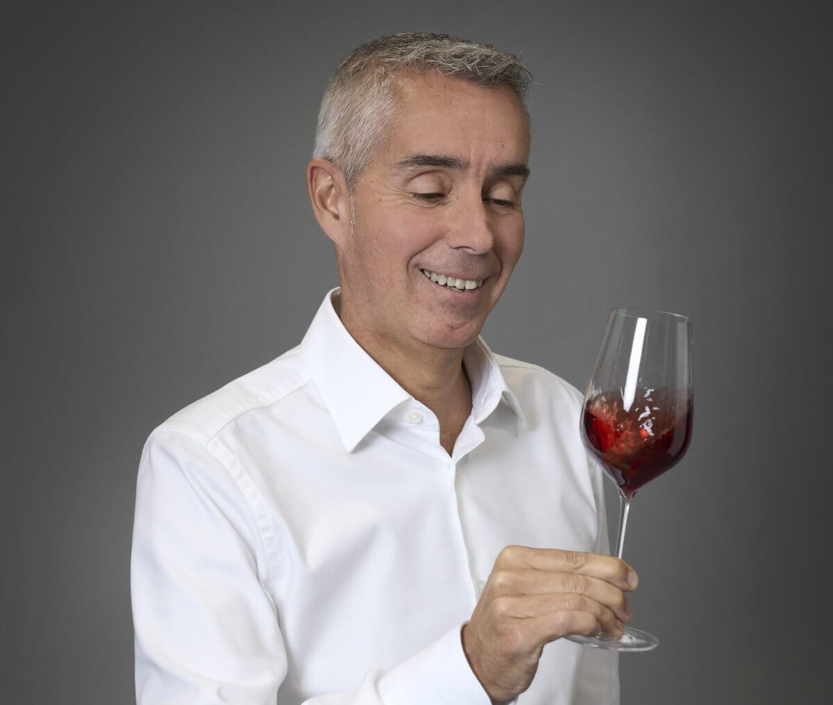 Sourire complice de Damien Delattre, co-fondateur de Sensation Vin, observant la robe d'un vin rouge avec passion et convivialité.